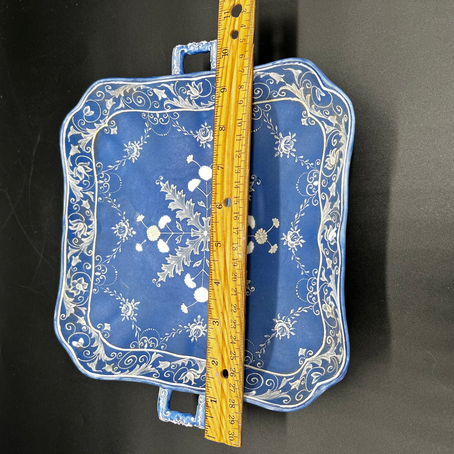 Blue tray with floral patterns and a wooden ruler for scale on a black background