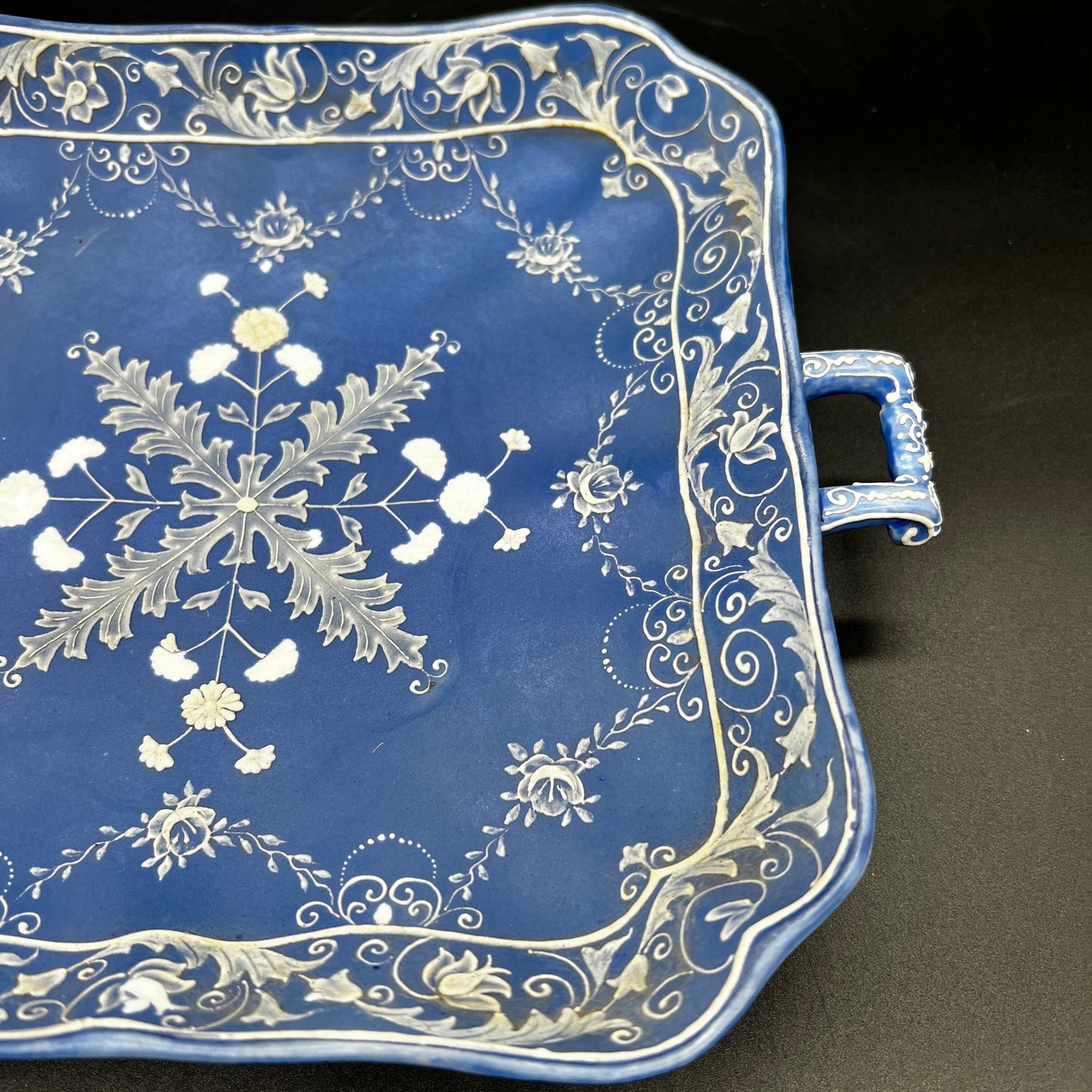 Decorative blue tray with white floral and leaf patterns on a black background