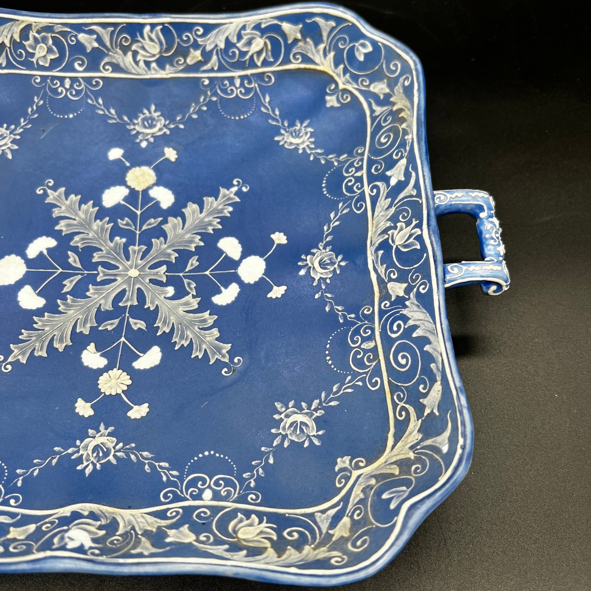 Decorative blue tray with white floral and leaf patterns on a black background