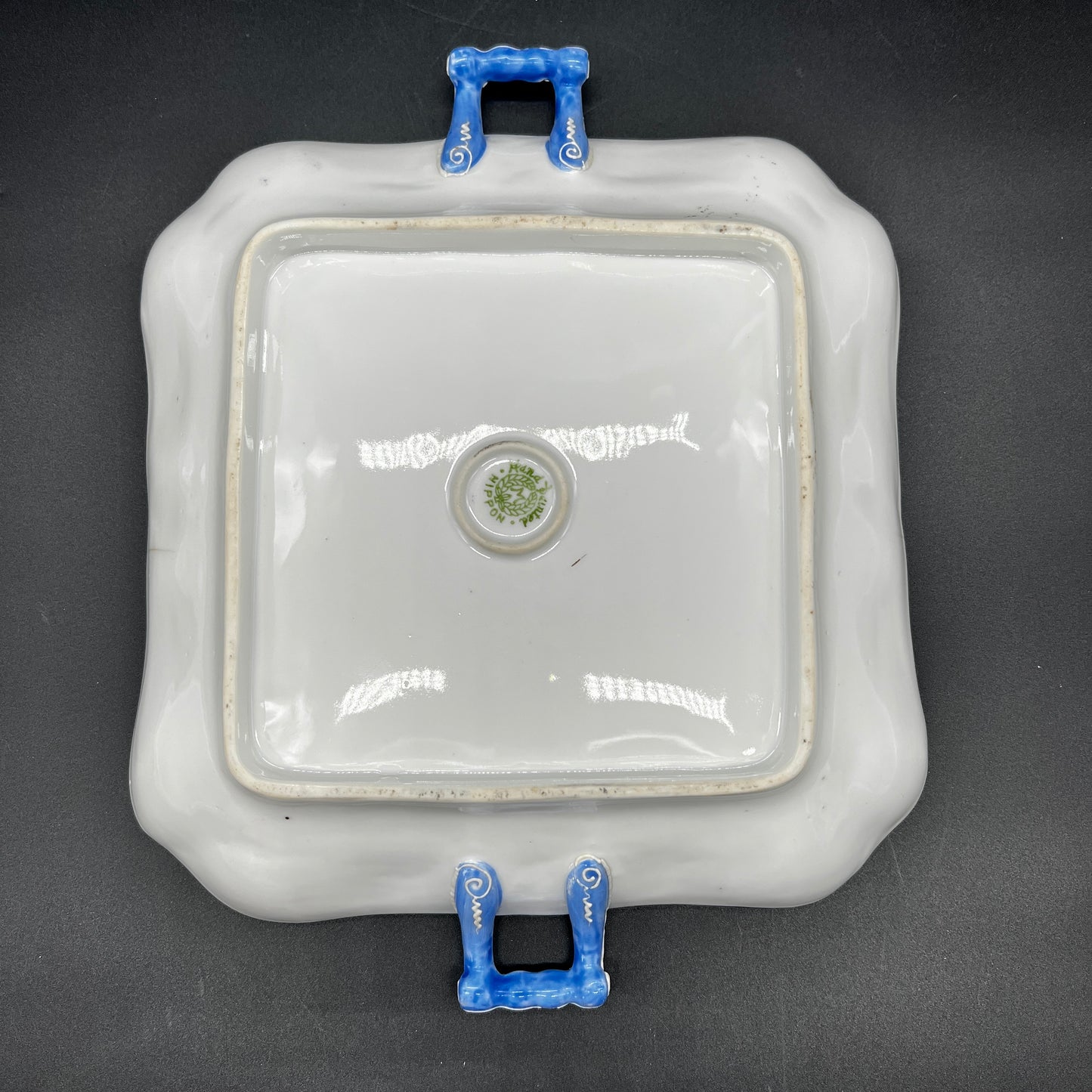 Square ceramic dish with blue handles on a black background