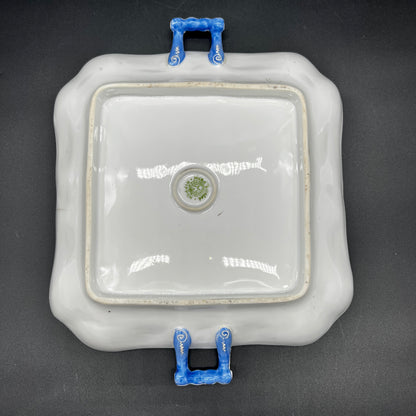 Square ceramic dish with blue handles on a black background