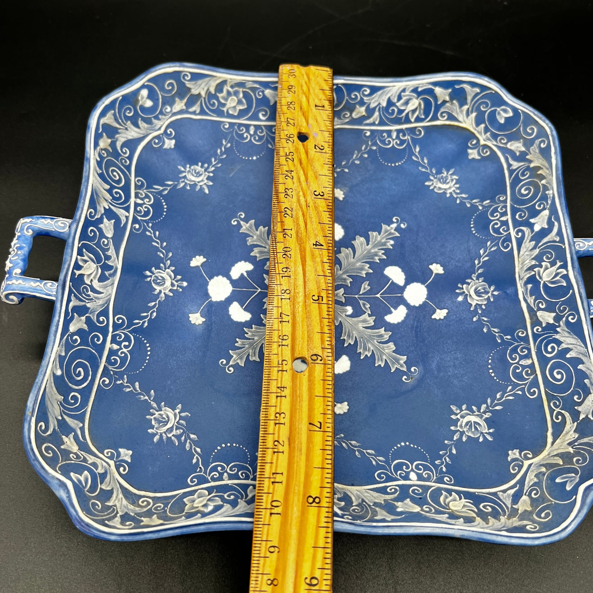 Decorative blue tray with white floral patterns and a ruler for scale on a black background