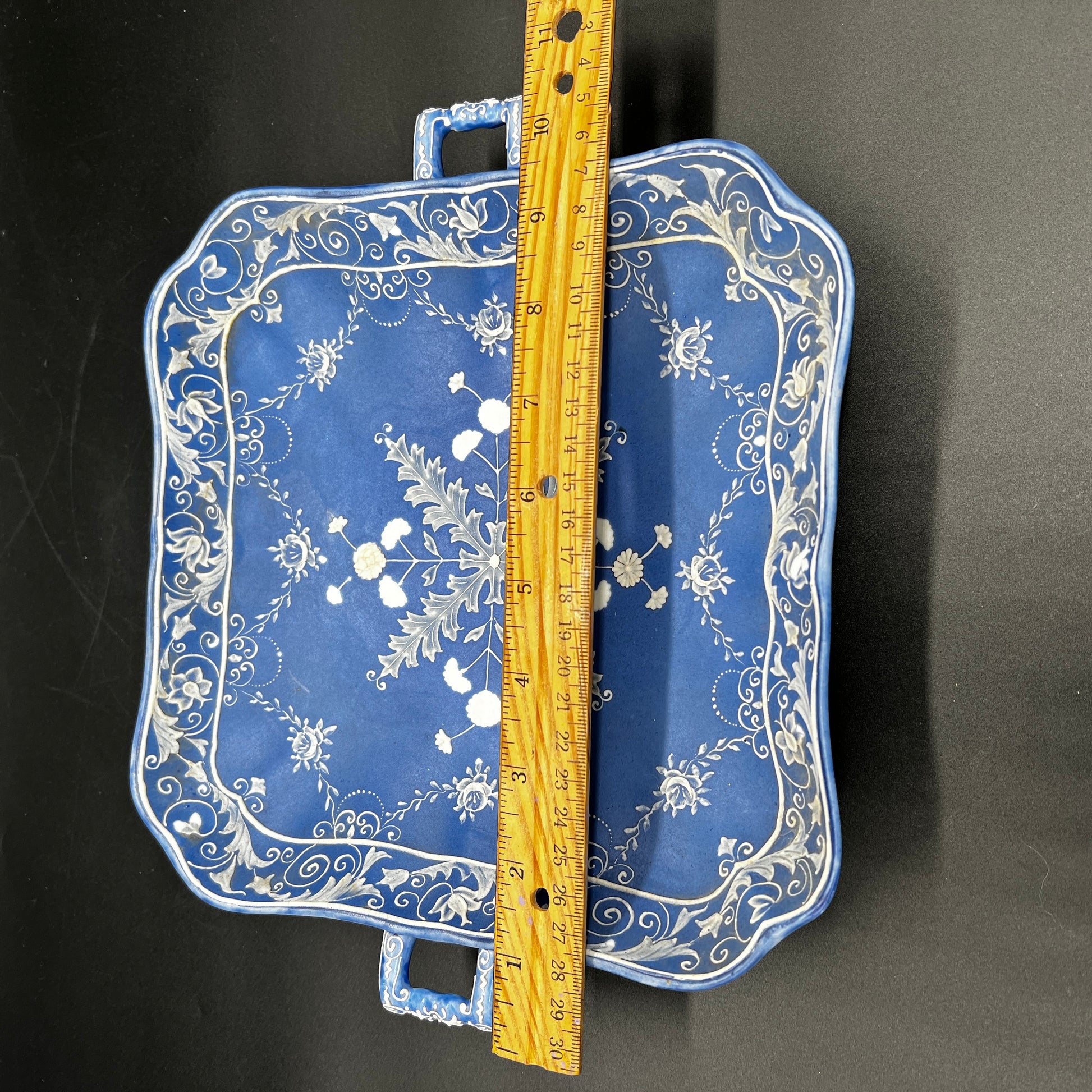 Blue tray with floral patterns and a wooden ruler for scale on a black background