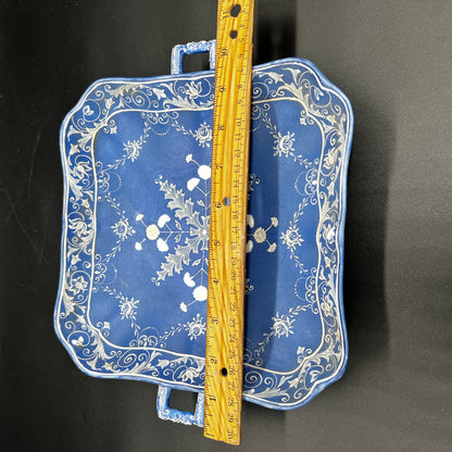 Blue tray with floral patterns and a wooden ruler for scale on a black background