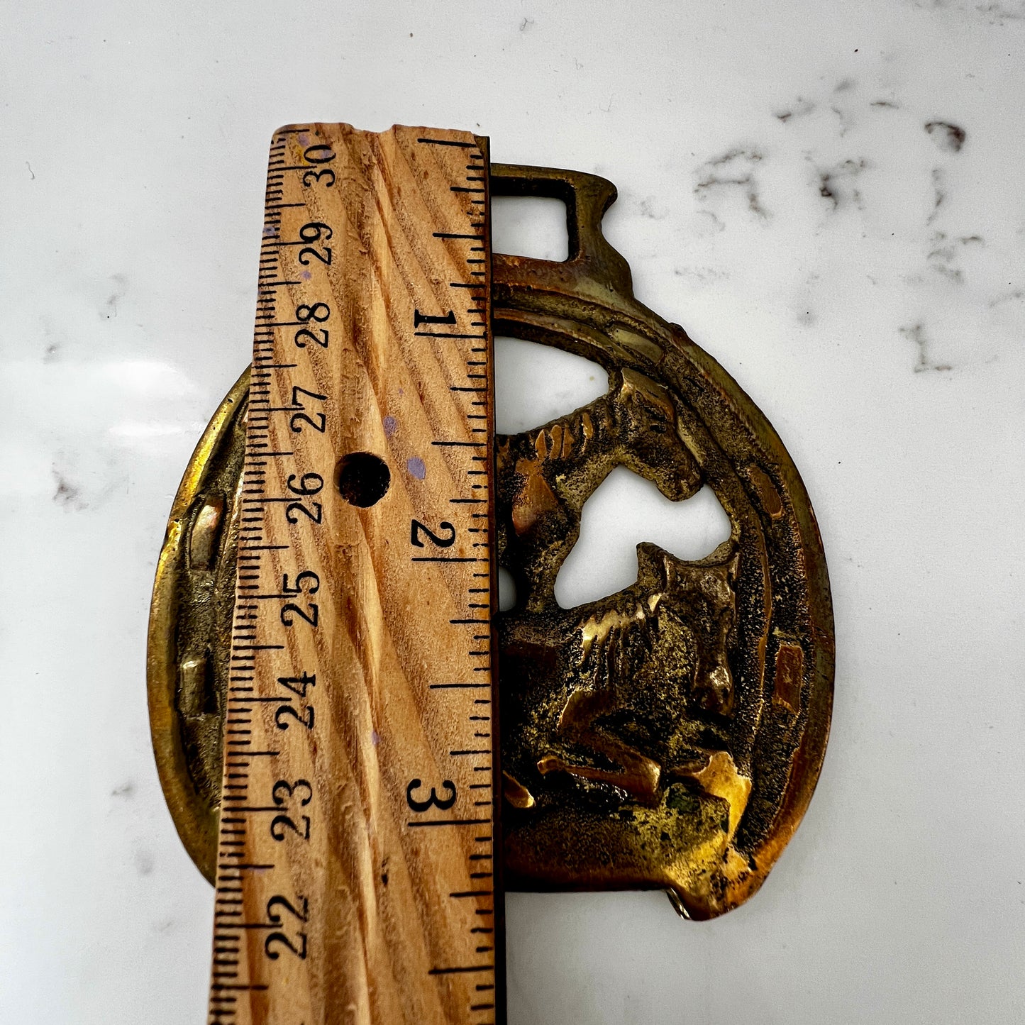 Decorative brass object with a ruler for scale on a marble surface