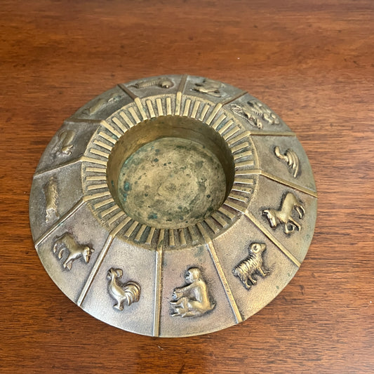 Decorative metal dish with zodiac symbols on a wooden surface
