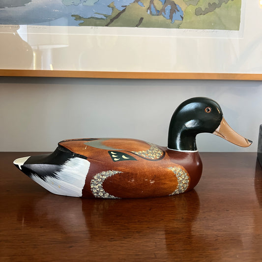 Wooden duck decoy on a wooden surface with a painting in the background