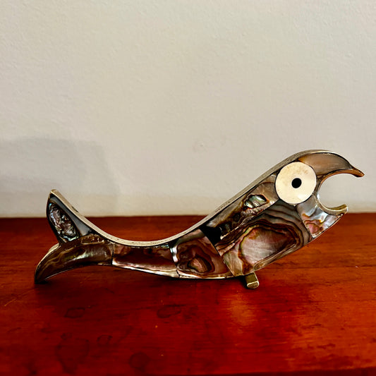 Metallic fish-shaped object on a wooden surface with a white background