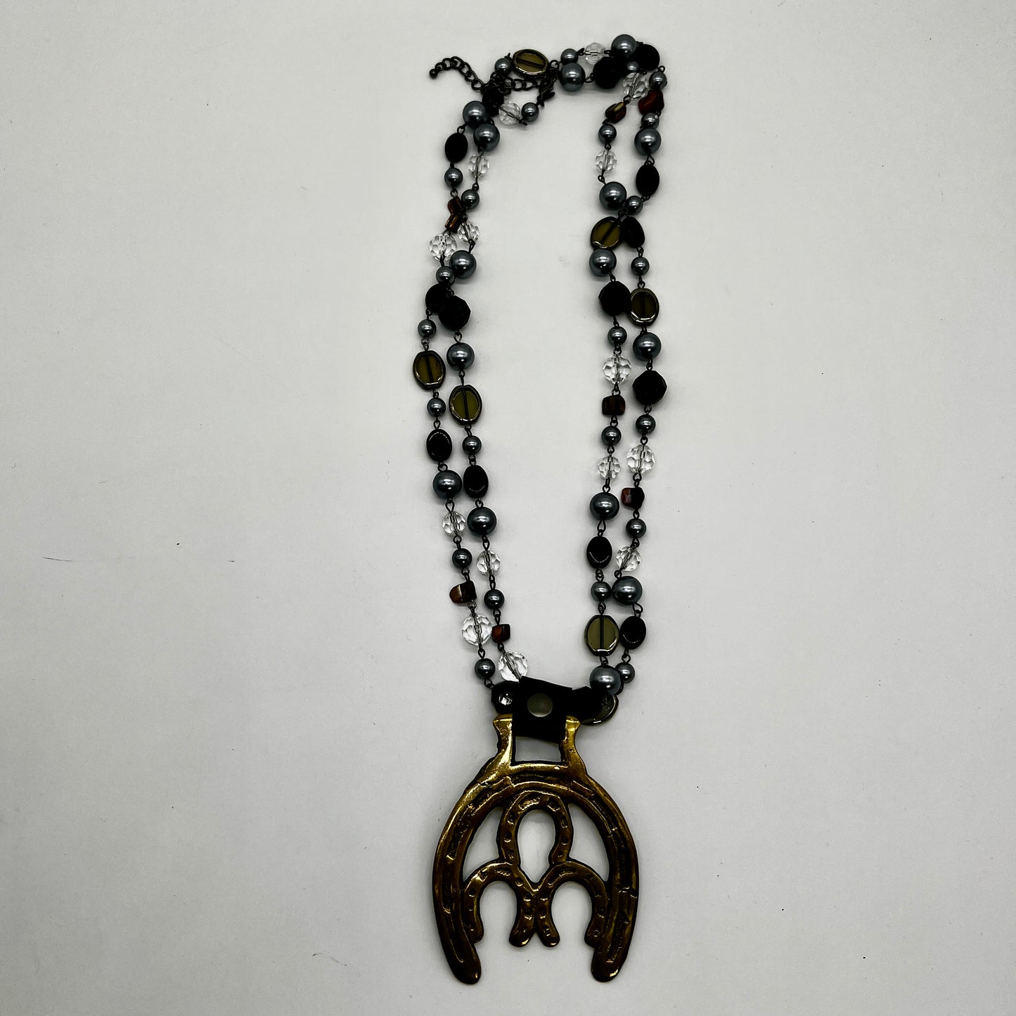 Vintage double horseshoe brass medallion necklace with dark multi-strand beads and leather connector.