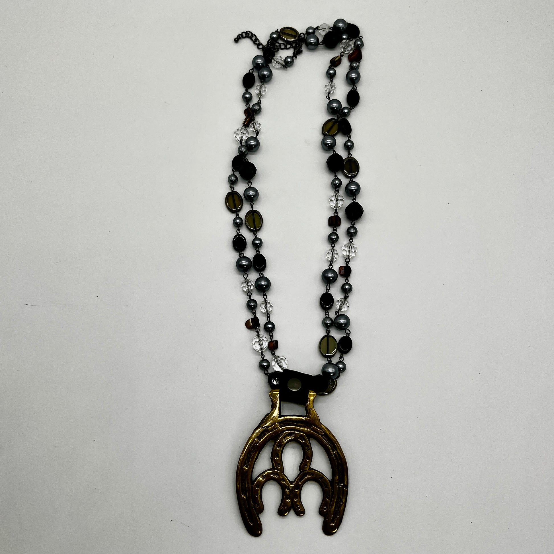 Vintage double horseshoe brass medallion necklace with dark multi-strand beads and leather connector.