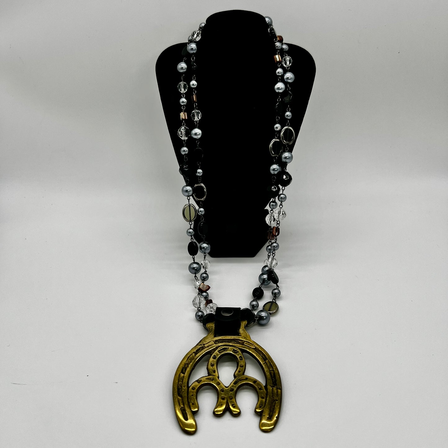 Vintage double horseshoe brass medallion necklace with dark multi-strand beads and leather connector.