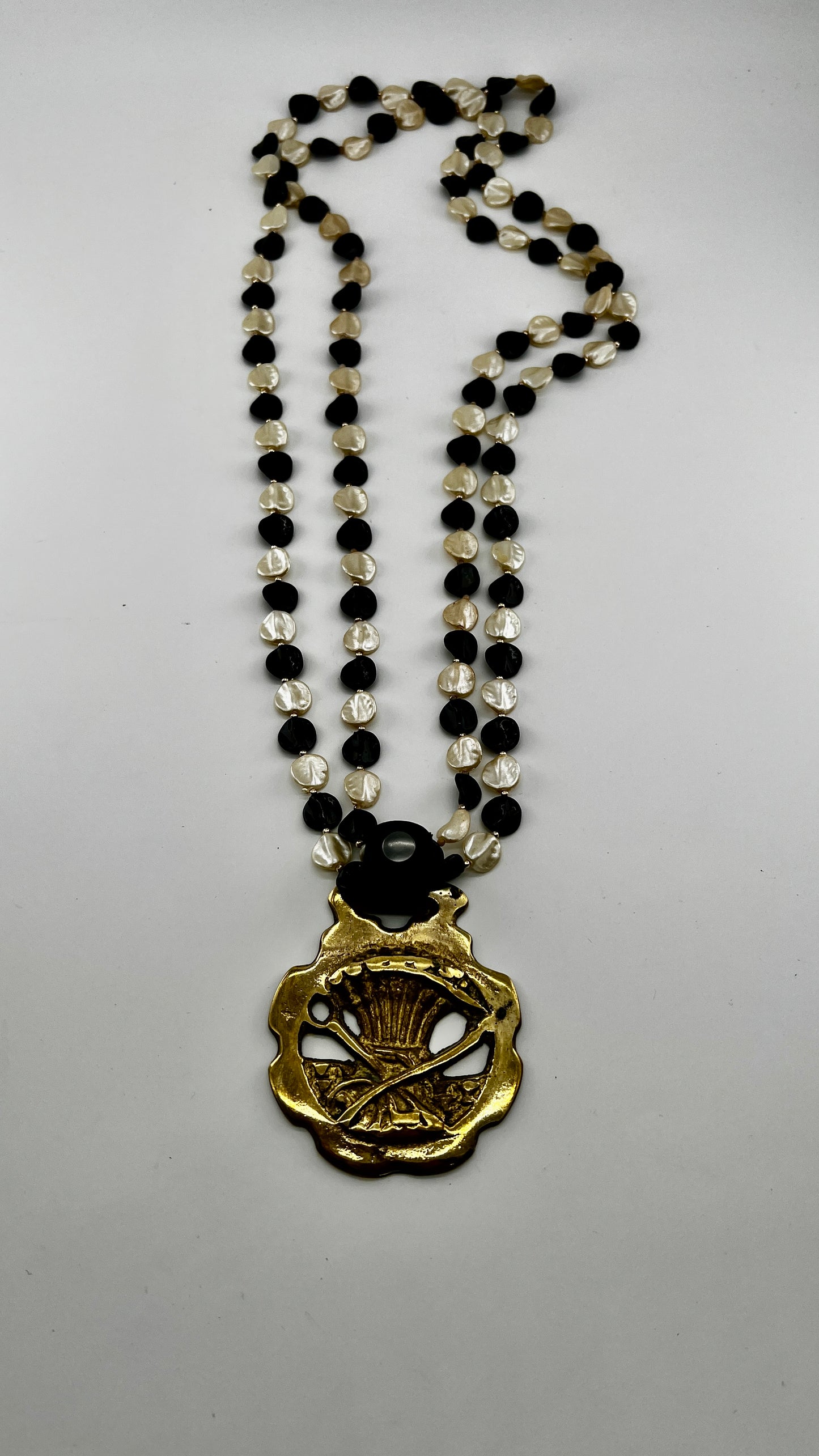 Vintage scythe and wheat horse brass medallion attached to triple-strand black and cream beaded necklace with leather connector.