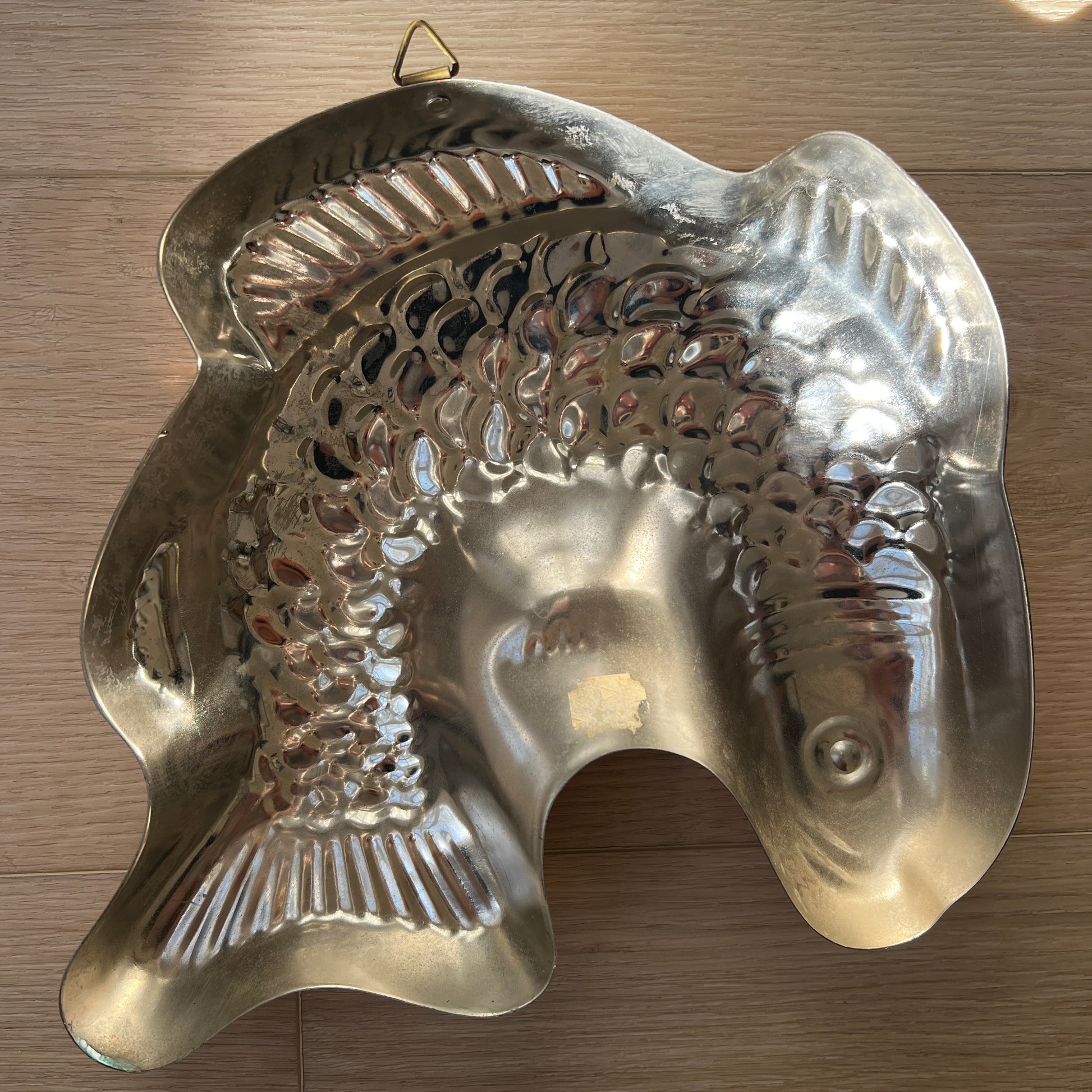 Back of vintage brass fish mold showing natural patina, hanging loop, and detailed fish design for farmhouse or nautical kitchen décor.