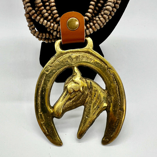 Vintage horse brass medallion attached to multi-strand wooden bead necklace with caramel leather connector.