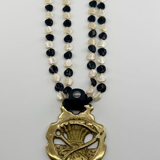 Vintage scythe and wheat horse brass medallion attached to triple-strand black and cream beaded necklace with leather connector.