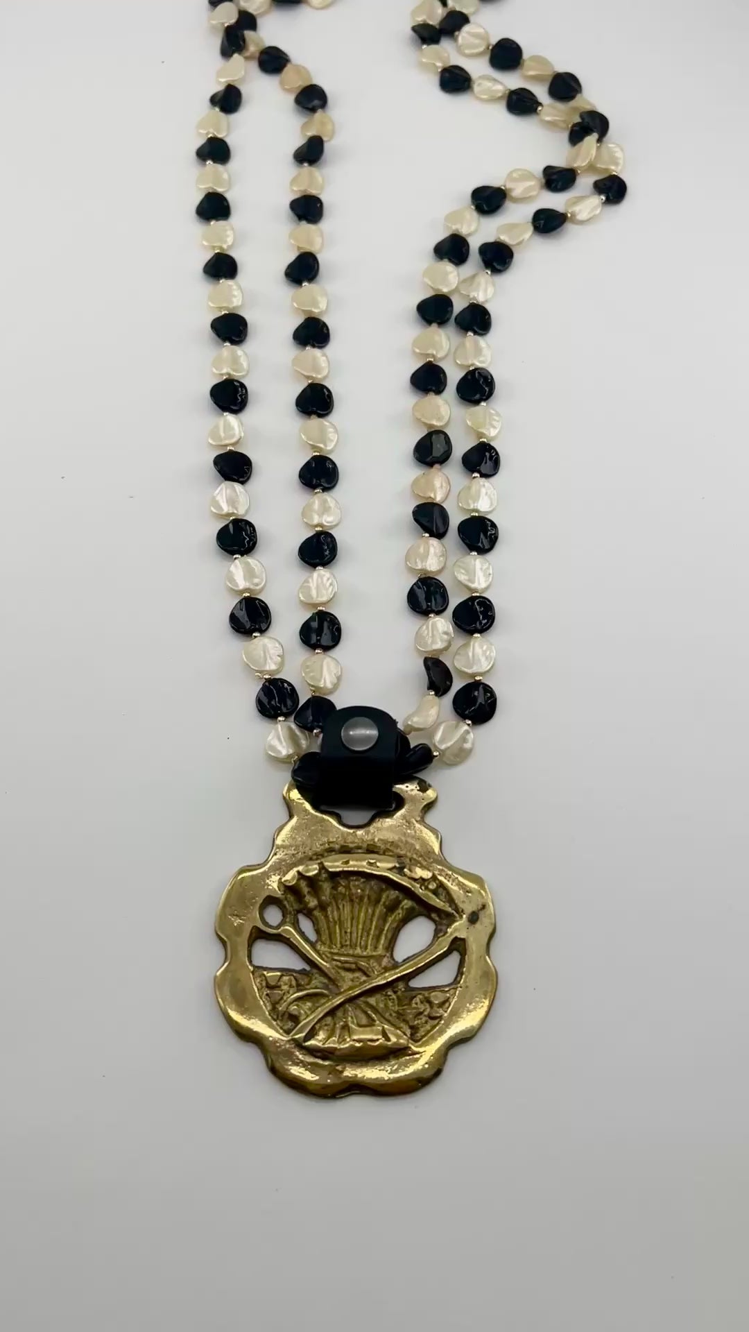 Vintage scythe and wheat horse brass medallion attached to triple-strand black and cream beaded necklace with leather connector.